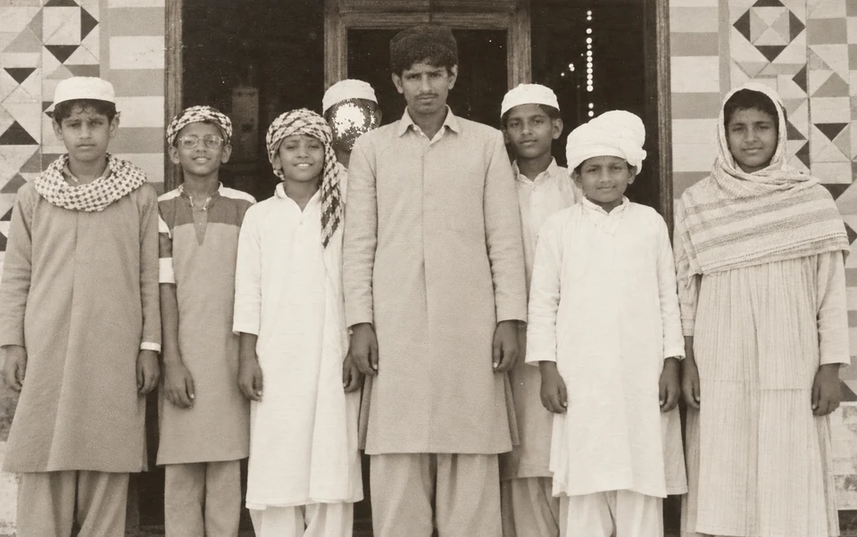 A group of students in traditional dress standing together outside a tiled entrance at the mosque.